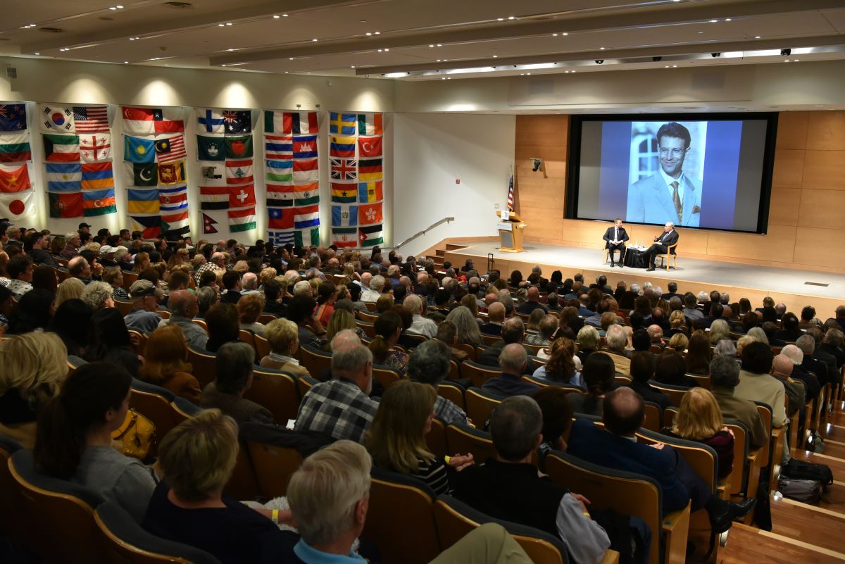 International conference setting featuring numerous national flags displayed behind an audience listening to a speaker presentation